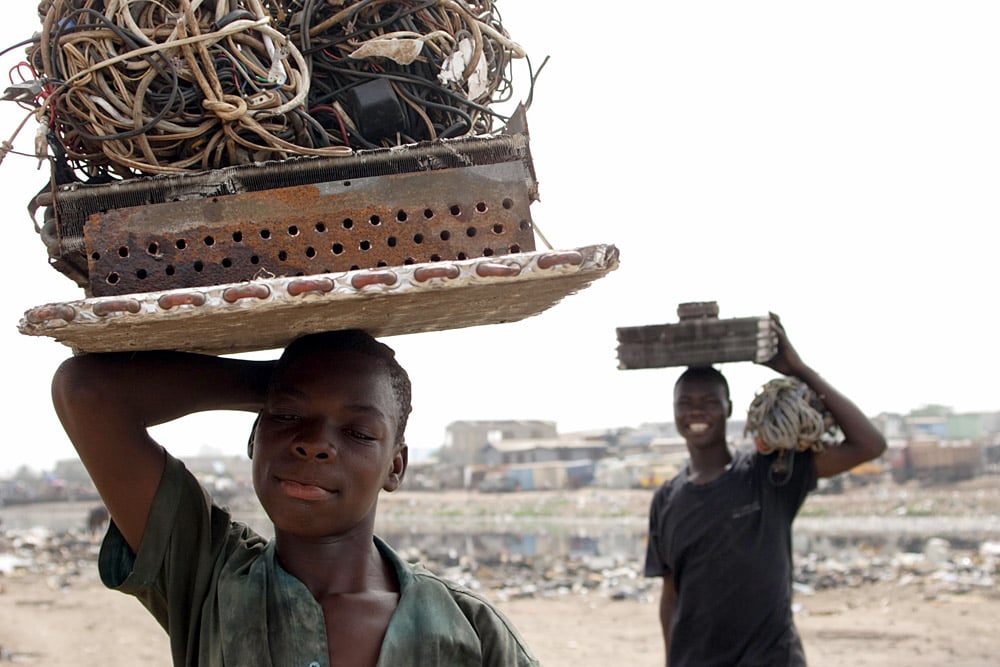 Boys carrying electronic cables from which they will extract the copper wiring by burning off the plastic in a small fire, Ghana, photo: Kate Davison/East News