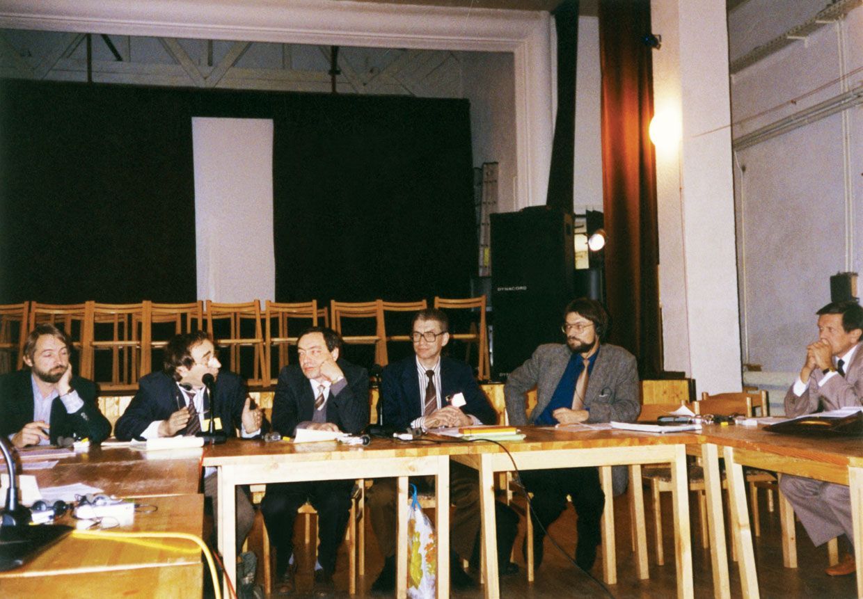Шестеро мужчин в костюмах за деревянными столами в конференц-зале