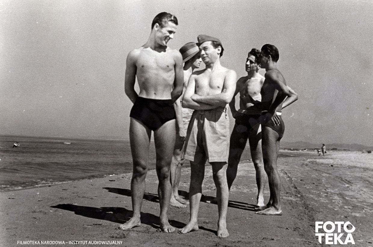 Grupa młodych ludzi w strojach kąpielowych rozmawiających na plaży